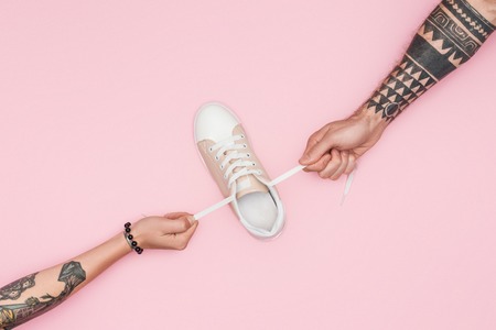 cropped view of tattooed shopaholics pulling sneaker isolated on pinkの写真素材
