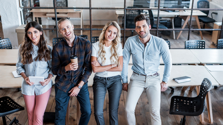 high angle view of happy young business people sitting and smiling at camera in officeの写真素材