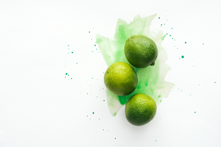 top view of whole three ripe limes on white surface with green watercolorの写真素材