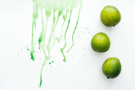 elevated view of whole limes on white surface with green watercolorの写真素材