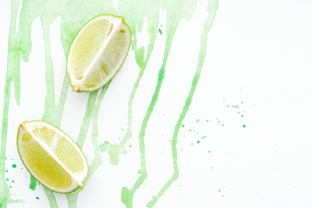 top view of two pieces of ripe limes on white surface with green watercolorの写真素材