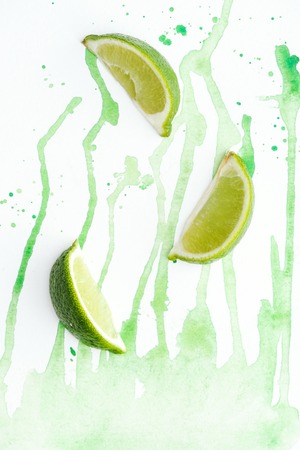 top view of pieces of organic limes on white surface with green watercolorの写真素材