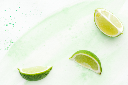top view of pieces of yummy limes on white surface with green watercolorの写真素材