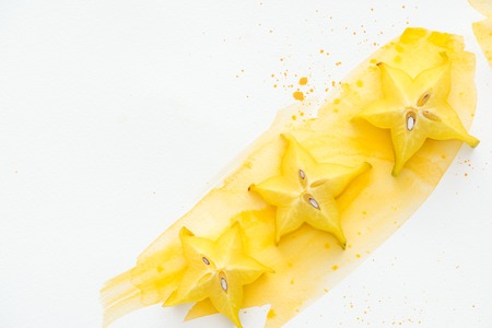 top view of three exotic star fruits on white surface with yellow watercolorの写真素材