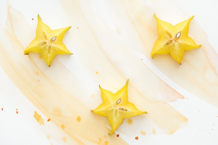 elevated view of three sweet star fruits on white surface with yellow watercolorの写真素材