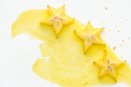 elevated view of tasty yellow star fruits on white surface with yellow watercolorの写真素材