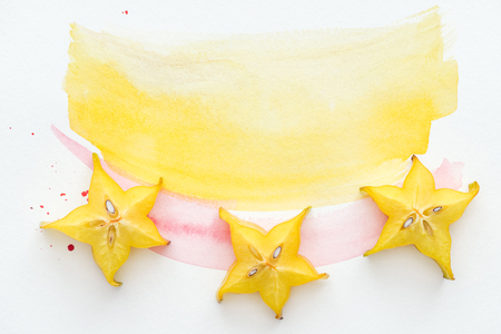 top view of sweet star fruits on white surface with yellow and pink watercolorsの写真素材
