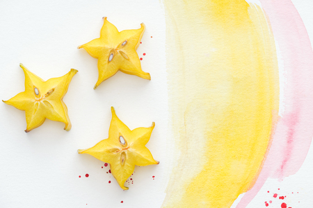 top view of three carambolas on white surface with yellow and pink watercolorsの写真素材