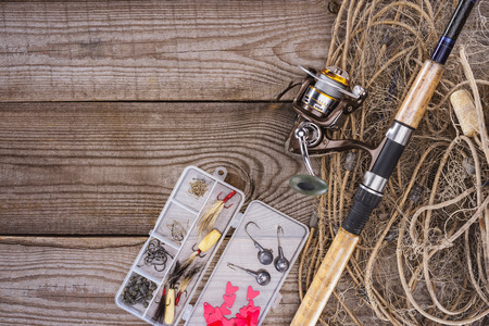 flat lay with fishing net, fishing rod and plastic box with fishing tackle and hooks on wooden planksの写真素材
