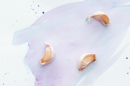 top view of pieces of spicy garlic on white surface with purple watercolor strokesの写真素材