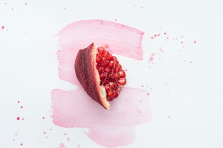 top view of piece of pomegranate on white surface with pink watercolor strokesの写真素材