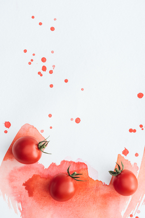 top view of cherry tomatoes on white surface with red watercolor strokes and blotsの写真素材