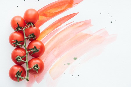 top view of branch of fresh cherry tomatoes on white surface with red watercolor strokesの写真素材