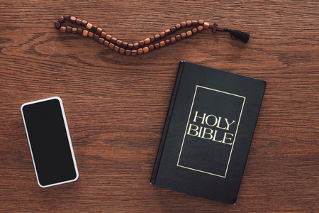 top view of holy bible with beads and smartphone on wooden tableの写真素材