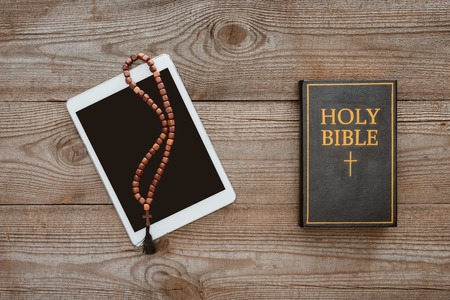 top view of tablet with beads and holy bible lying on wooden table