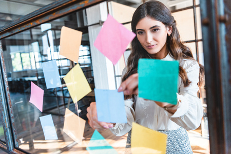 beautiful young businesswoman working with colorful sticky notes in officeの写真素材
