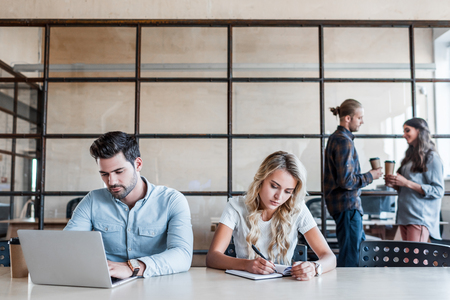 young business people working at workplace while colleagues drinking coffee behindの写真素材