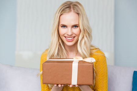 attractive blonde holding gift box and smiling at cameraの写真素材