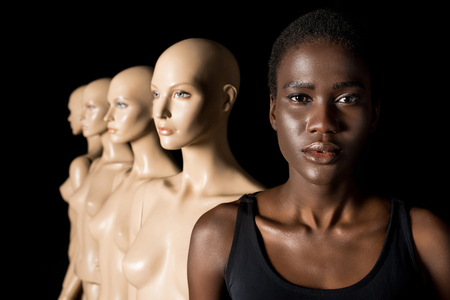 serious african american girl looking at camera while standing with dummies on black
