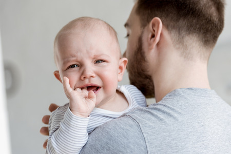 father holding little crying baby boy at homeの写真素材