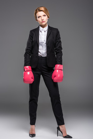 serious businesswoman posing in suit and pink boxing gloves, isolated on greyの写真素材