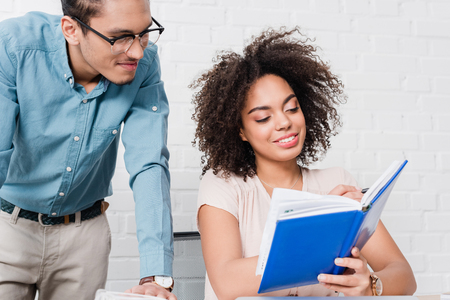 Businessman looking at woman writing in notebook in officeの写真素材