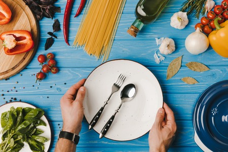 cropped image of man putting plate with fork and spoon on blue tableの写真素材