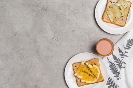 top view of healthy toasts with honey and slices of fruits and glass of fresh juice on greyの写真素材