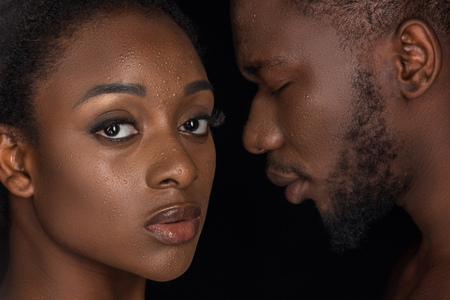 beautiful african american couple with water drops on faces posing isolated on blackの写真素材