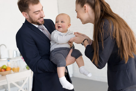 smiling business parents in formal wear holding baby at homeの写真素材