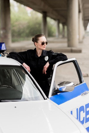 attractive female police officer standing near patrol carの写真素材