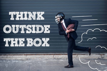 side view of businessman in suit and rugby helmet with ball in hands running on street with think outside box inscriptionの写真素材