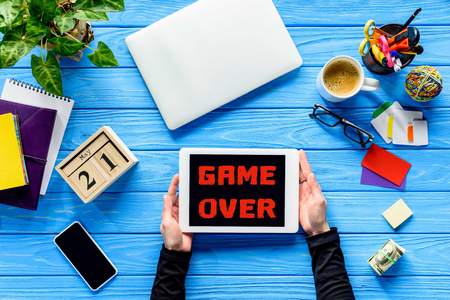 hands holding tablet on blue wooden table with money and stationery, Game over letteringの写真素材
