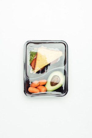 top view of closed plastic lunch box with sandwich and vegetables isolated on whiteの写真素材