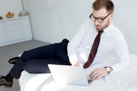businessman in eyeglasses using laptop in bedroomの写真素材