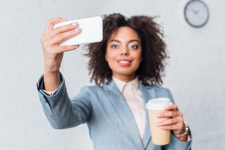 Businesswoman in suit holding coffee cup and taking selfieの写真素材