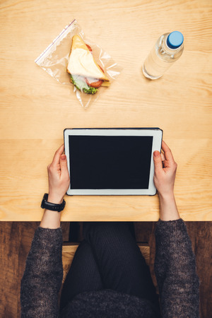 cropped image of woman sitting at table with sandwich in ziplock bag and using tabletの写真素材