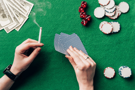 Woman holding cigarette and playing cards by casino tableの写真素材