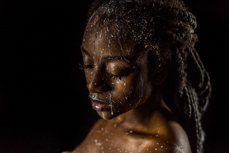 close-up view of seductive african american girl with milk drops on face and body isolated on blackの写真素材