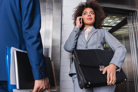 Businesswoman with briefcase talking on the phone next to man by elevatorの写真素材