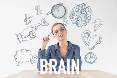 thoughtful businesswoman sitting at table and holding pencil in hand, with business icons and brain inscriptionの写真素材