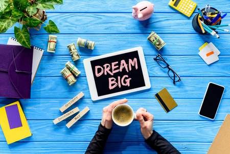 Hands holding coffee cup on blue wooden table by money and digital tablet, Dream big inspiration