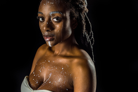 sensual young african american woman with spilled milk on face looking at camera isolated on blackの写真素材