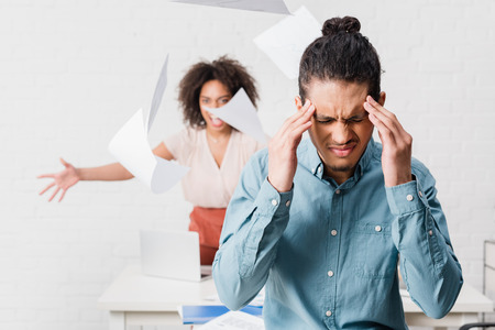 Businessman suffering from headache while his female colleague yelling in officeの写真素材