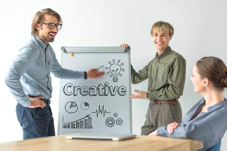 Laughing businessmen showing creative inscription and business signs on flipchat to businesswoman