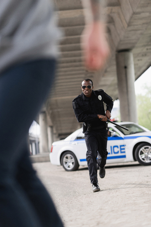 cropped shot of thief running from african american policemanの写真素材