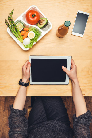 cropped image of woman sitting at table with food in container and using tabletの写真素材