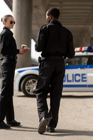 smiling police officers having coffee break and chatting in front of carの写真素材