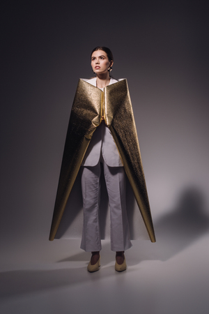 stylish woman in white suit covered in golden wrapping paper posing on dark backgroundの写真素材
