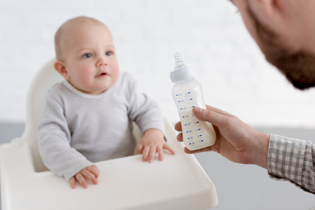 father feeding little baby boy with milk on kitchen